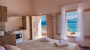 Une chambre avec un grand lit, une table de chevet, une lampe et une vue sur la mer par une porte ouverte.
