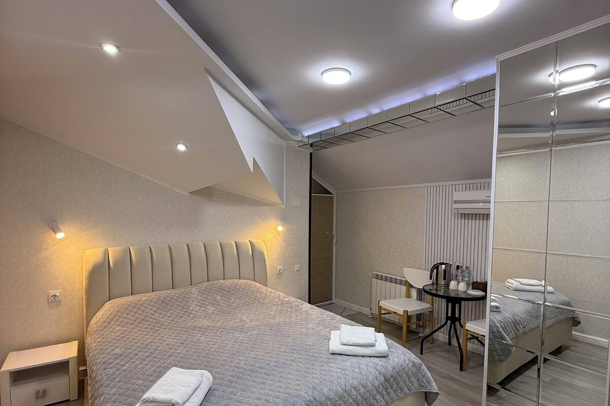 Een moderne slaapkamer met een groot bed, nachtkastjes, een klein bureau en een spiegel.