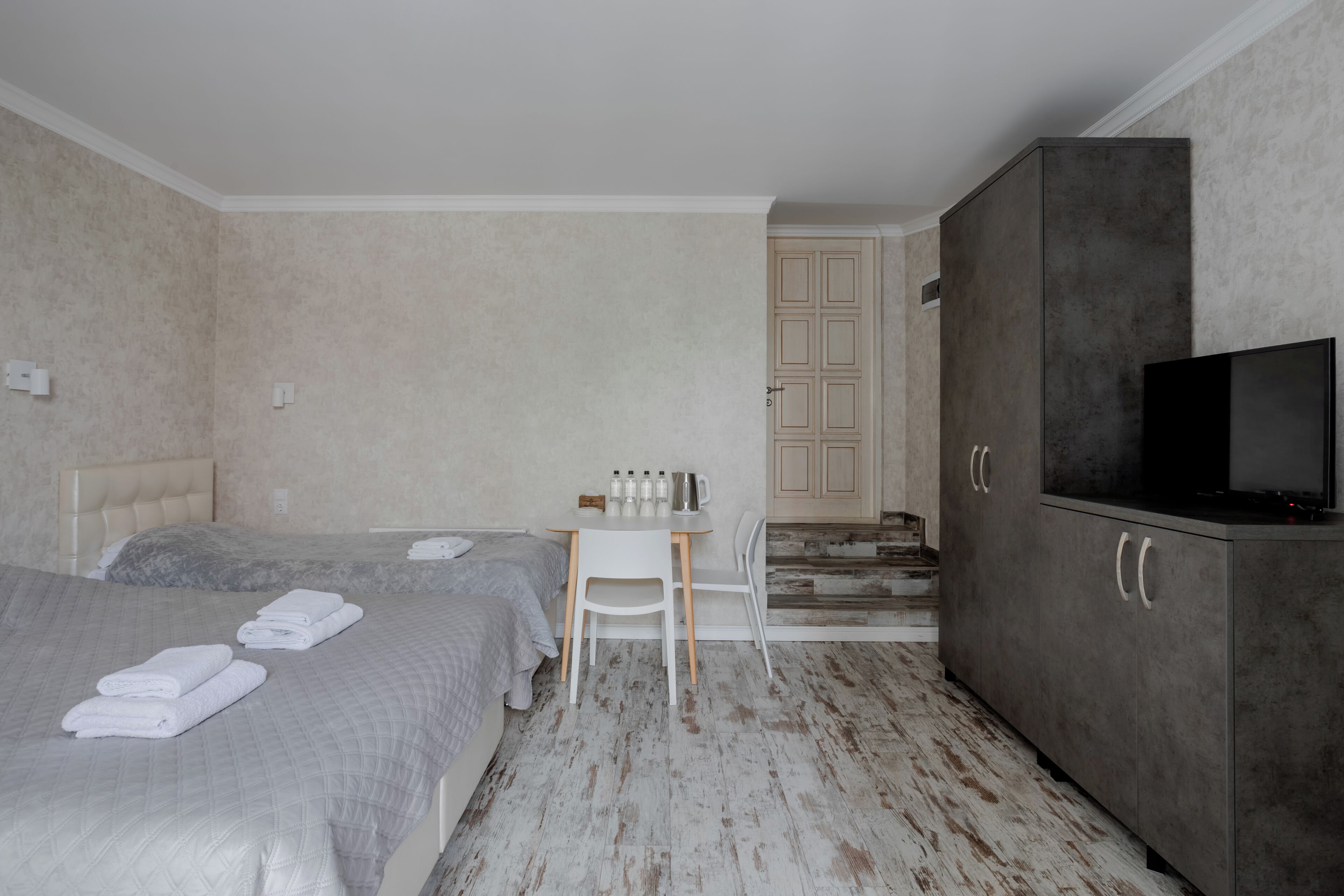 Quarto de hotel com duas camas, uma escrivaninha, uma televisão e um guarda-roupa.