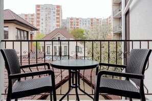 A balcony with two wicker chairs and a round table, overlooking a residential area with apartment buildings and a small house. - Hotel Kalyan & Spa (Chisinau)