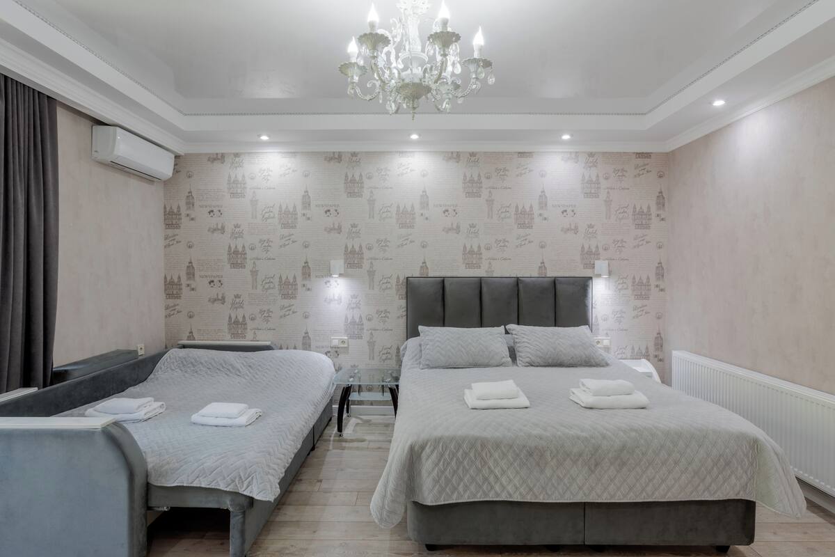 Een hotelkamer met twee bedden, een kroonluchter, een radiator en behang met een patroon.