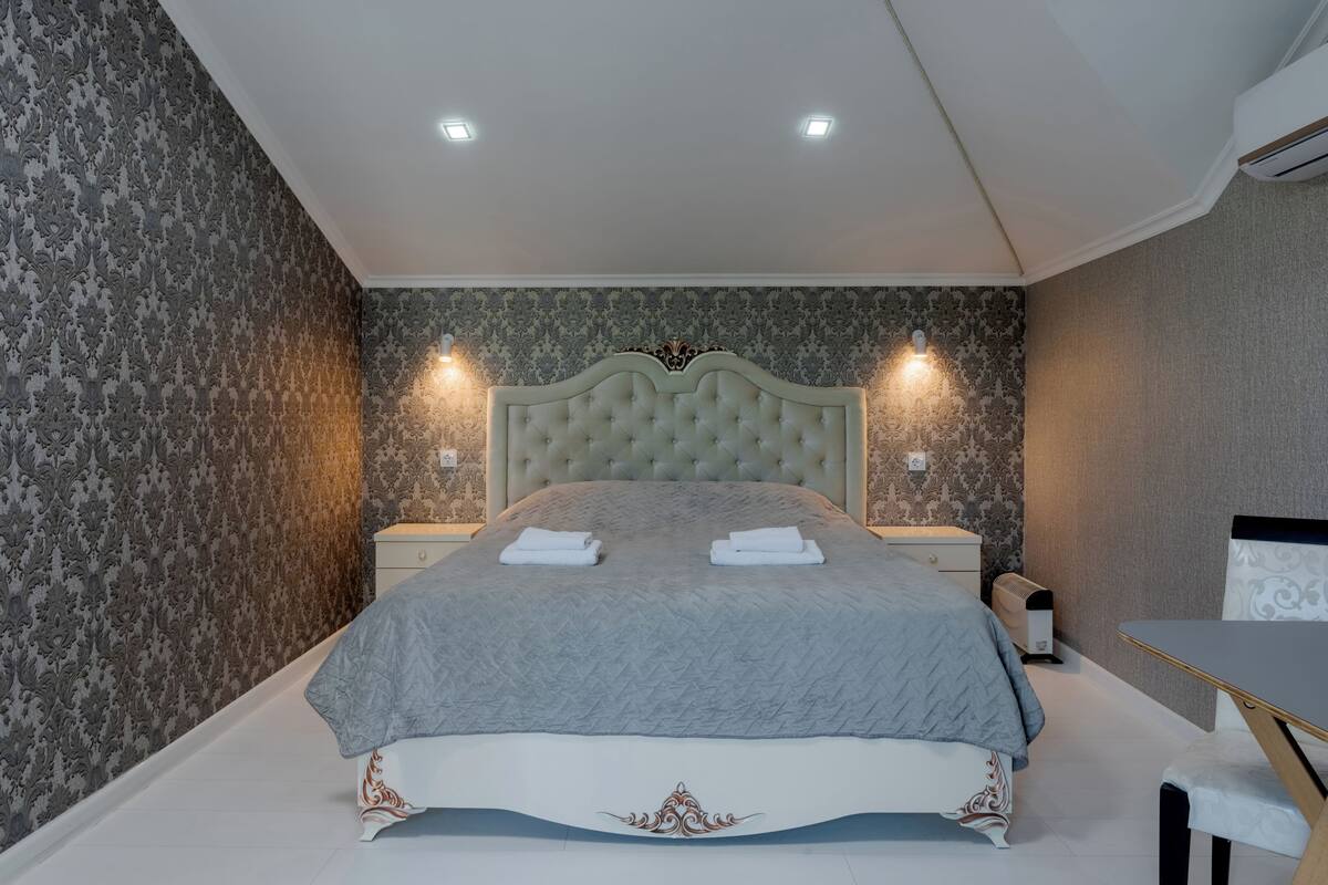 Een slaapkamer met een groot bed, twee nachtkastjes, een bijzettafeltje en een bureau met stoel.
