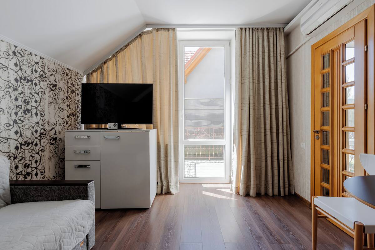Een slaapkamer met een bed, een televisie, een kledingkast, een bureau en een balkon met gordijnen.