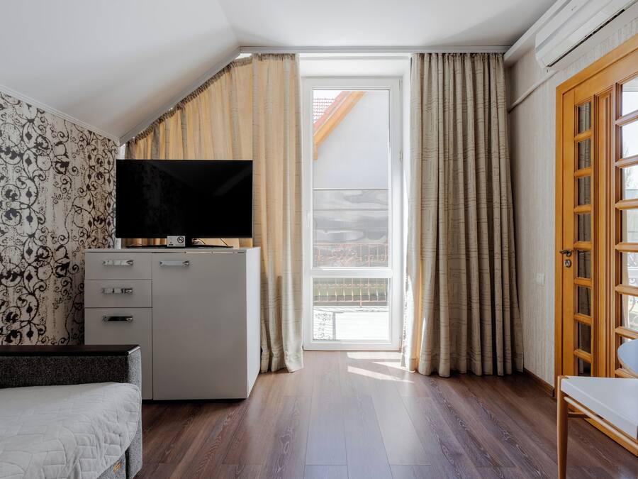 A bedroom with a bed, a TV, a wardrobe, a desk, and a balcony with curtains.