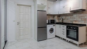 A modern kitchen with white cabinetry, a stainless steel refrigerator, a washing machine, and a black oven.