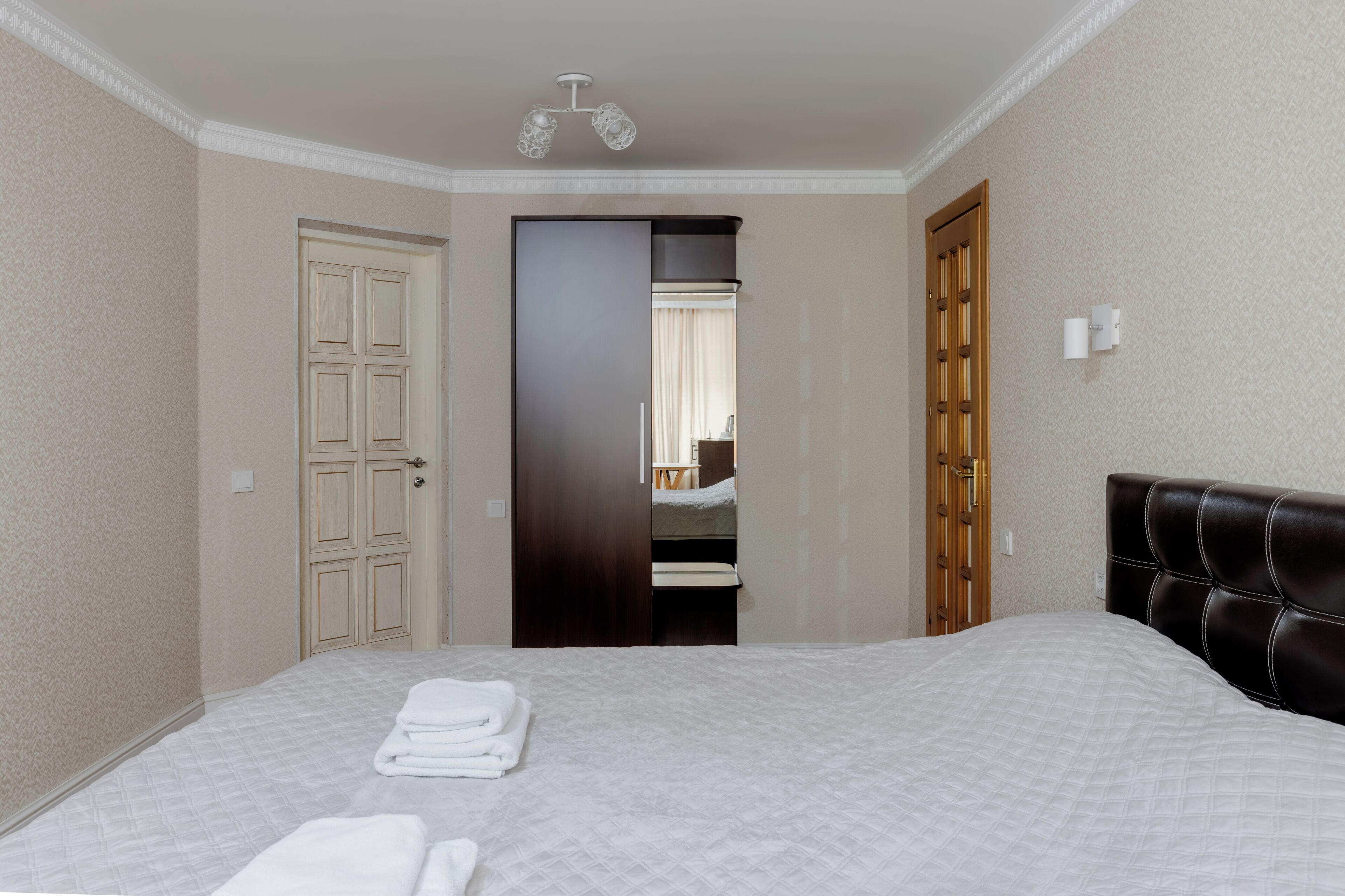 A hotel room with a bed, a wardrobe, a mirror, and a door leading to another room.