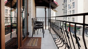 A balcony with a view of a cityscape, a set of chairs, and a doormat.