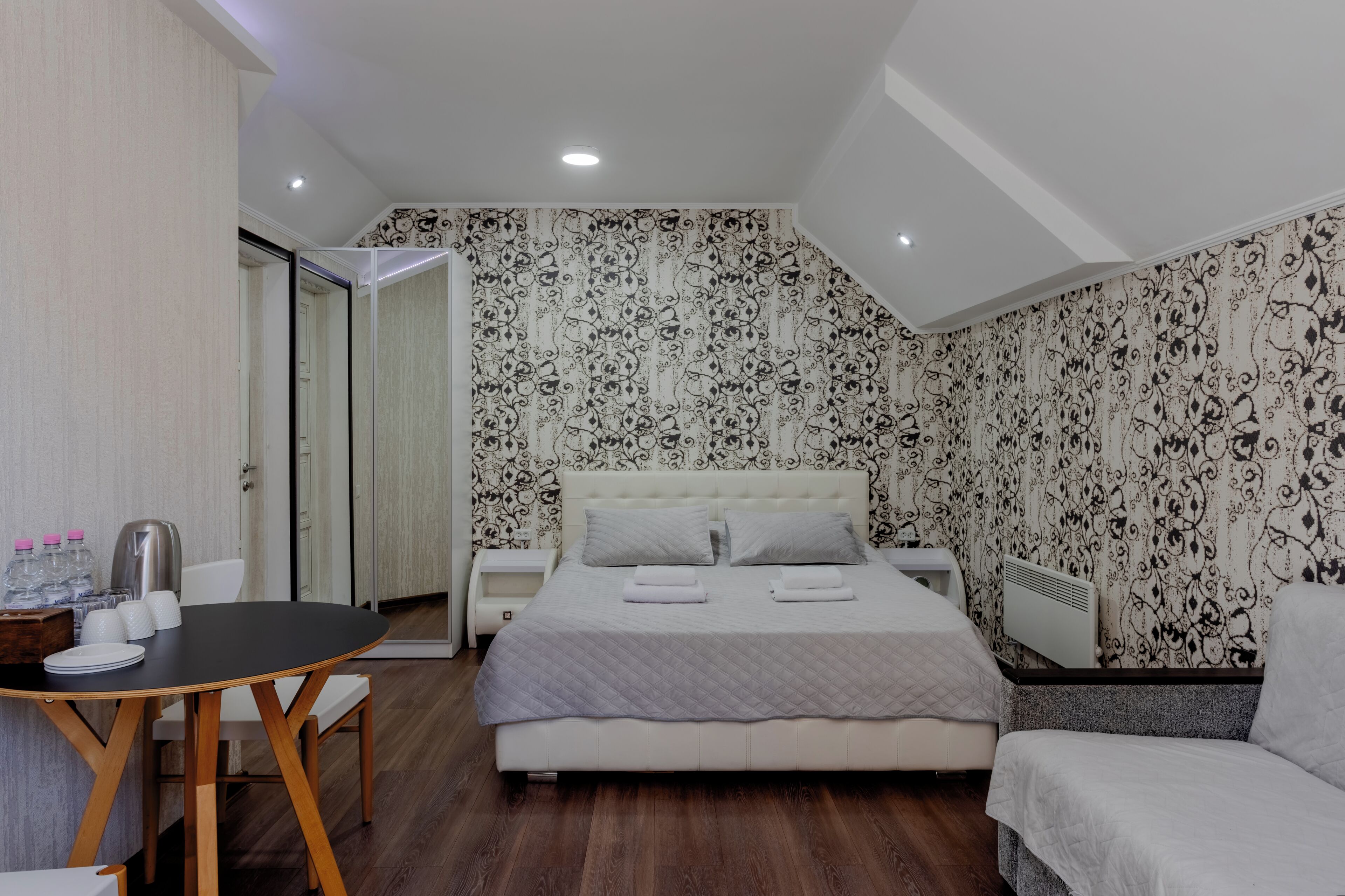 Un dormitorio con cama, mesitas de noche, un escritorio con sillas y un espejo.