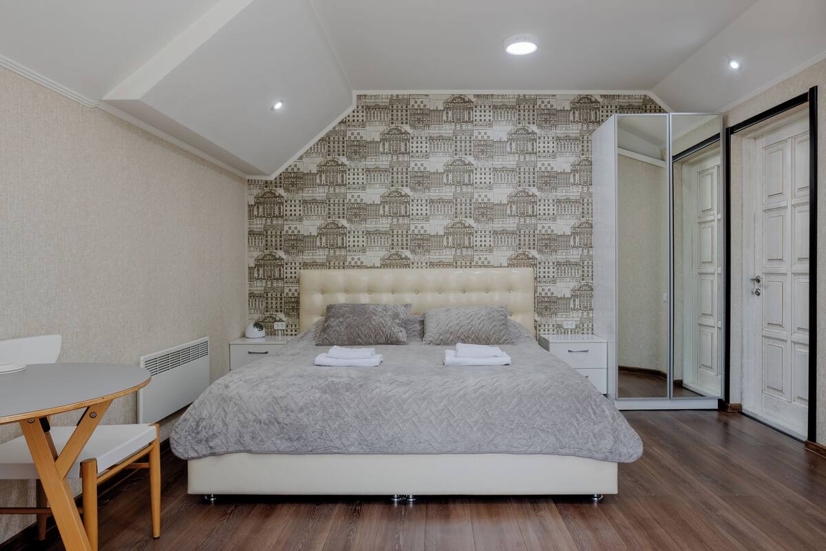 Een moderne slaapkamer met een groot bed, nachtkastje, stoel en spiegel.