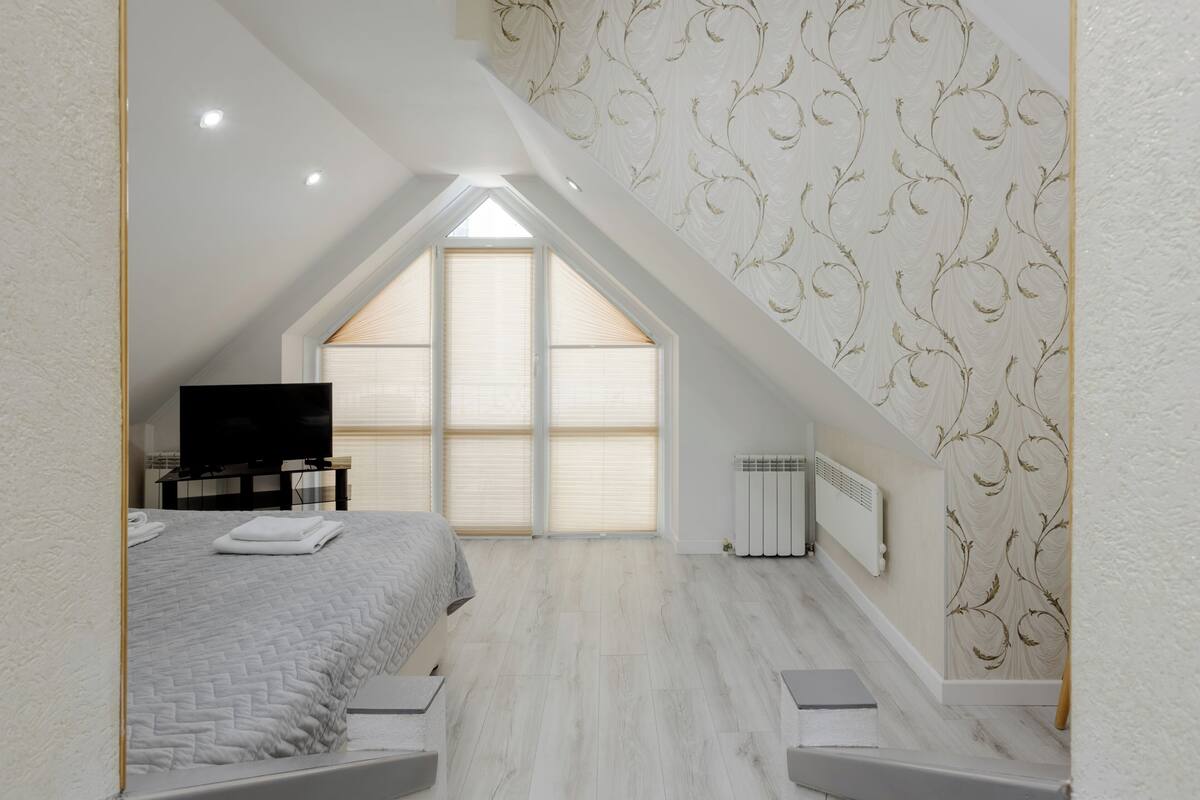 Een slaapkamer met een schuine kap, een bed, een televisietoestel en een raam met zonwering.