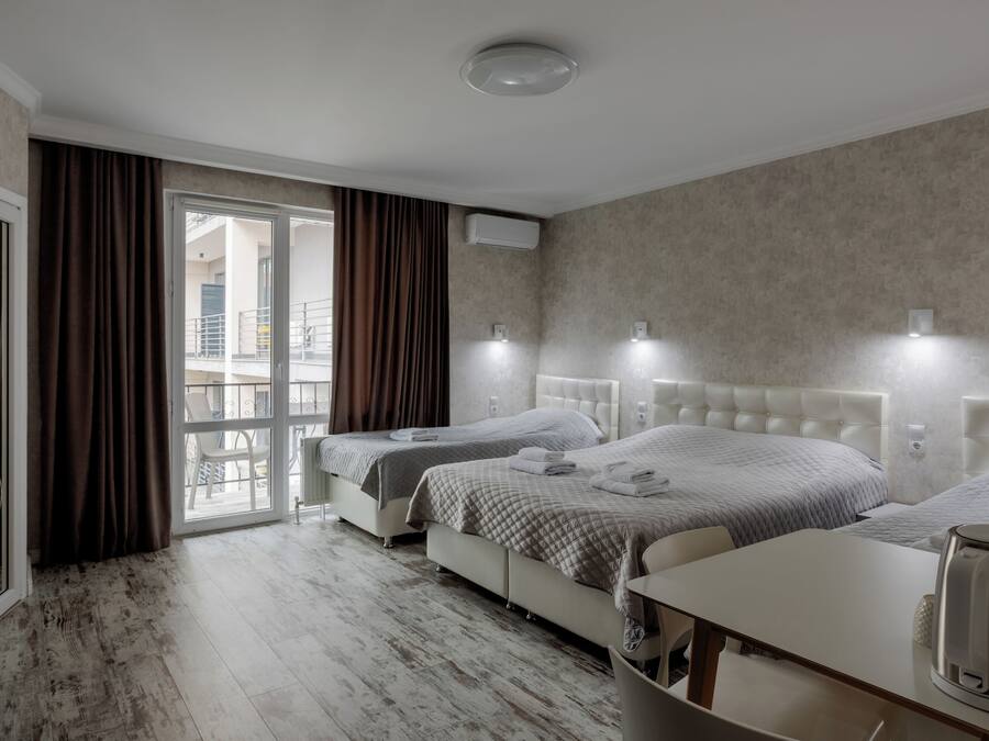 A hotel room with two beds, a balcony, a coffee maker, and a view of the outside.