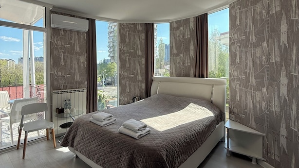 A modern bedroom with a large bed, a chair, a small table, and a view of the city.