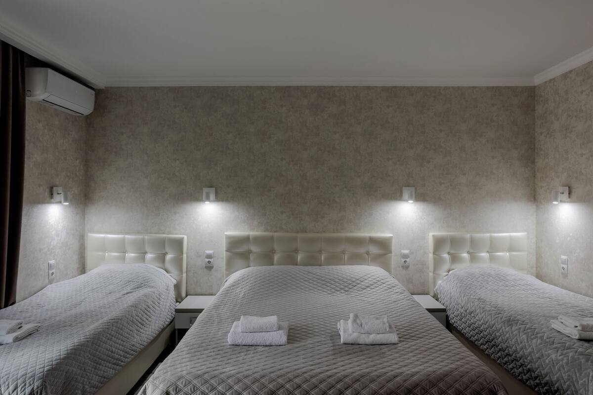 Een hotelkamer met drie bedden, elk voorzien van een hoofdeinde en bedlampjes.