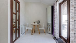 A narrow hallway with a wooden door, a white radiator, a round table with two chairs, and a window with newspaper-patterned curtains.