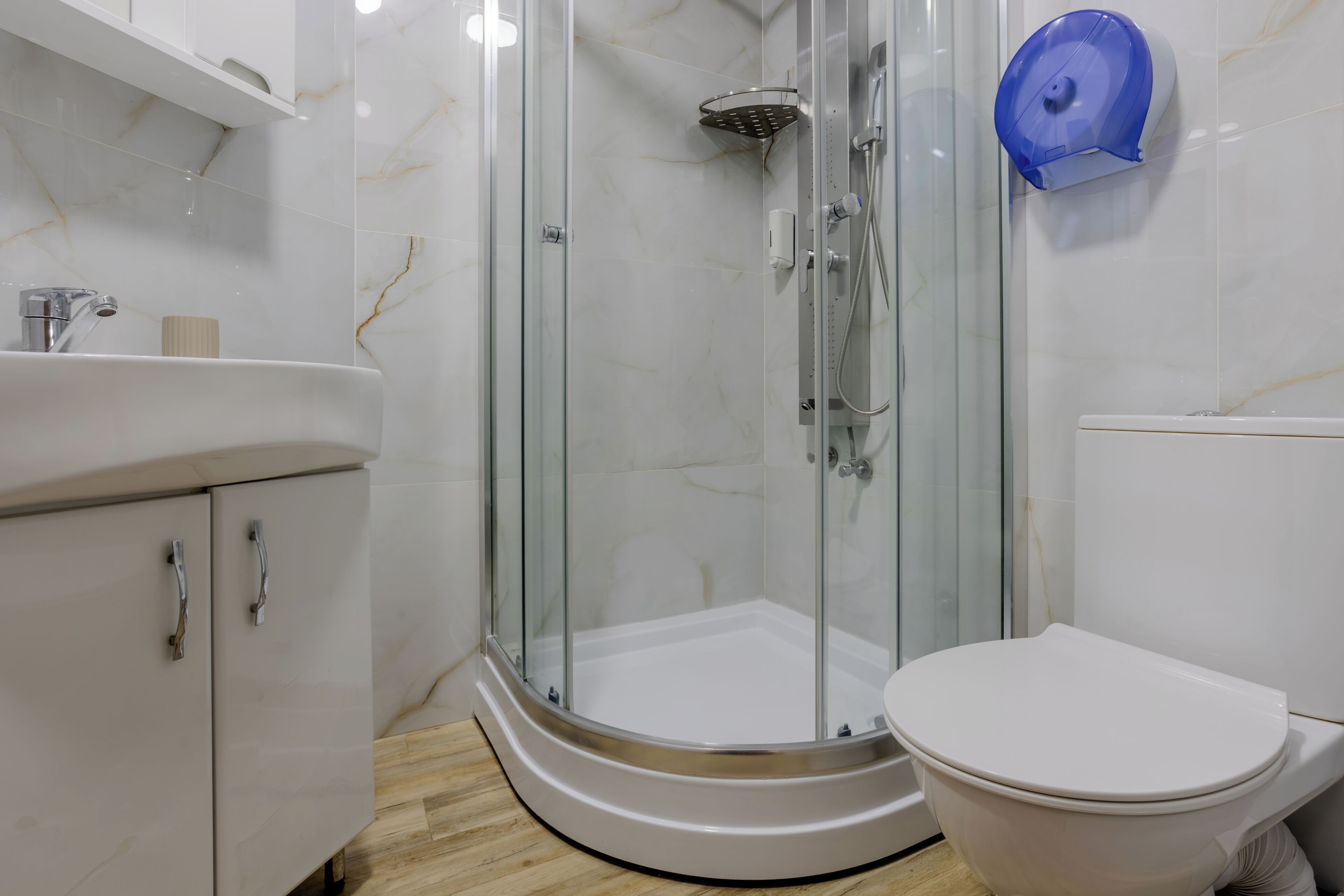 Baño con ducha envuelta en vidrio, inodoro y lavamanos con encimera de mármol.