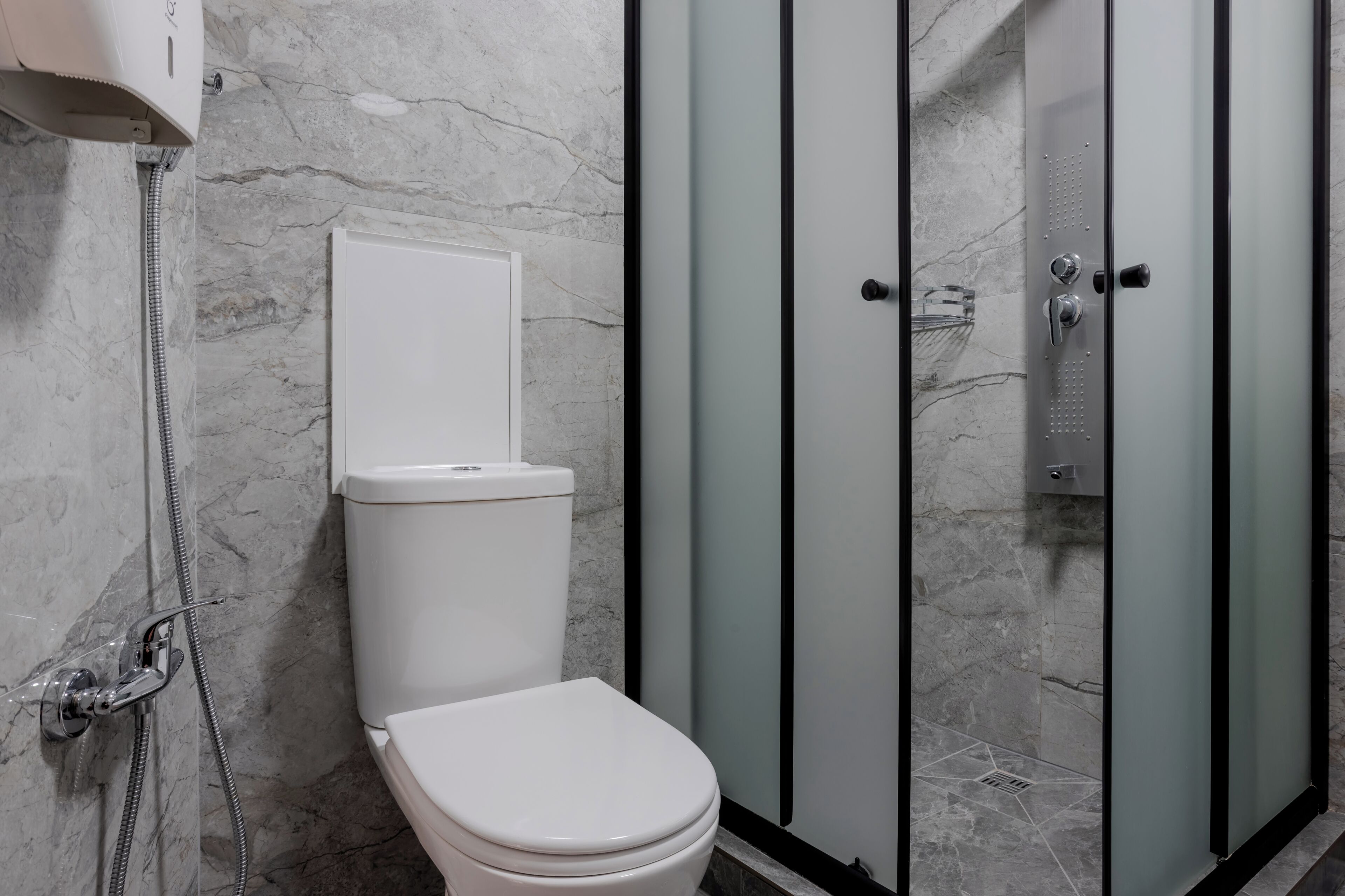 A bathroom with a toilet, shower enclosure, and marble walls.