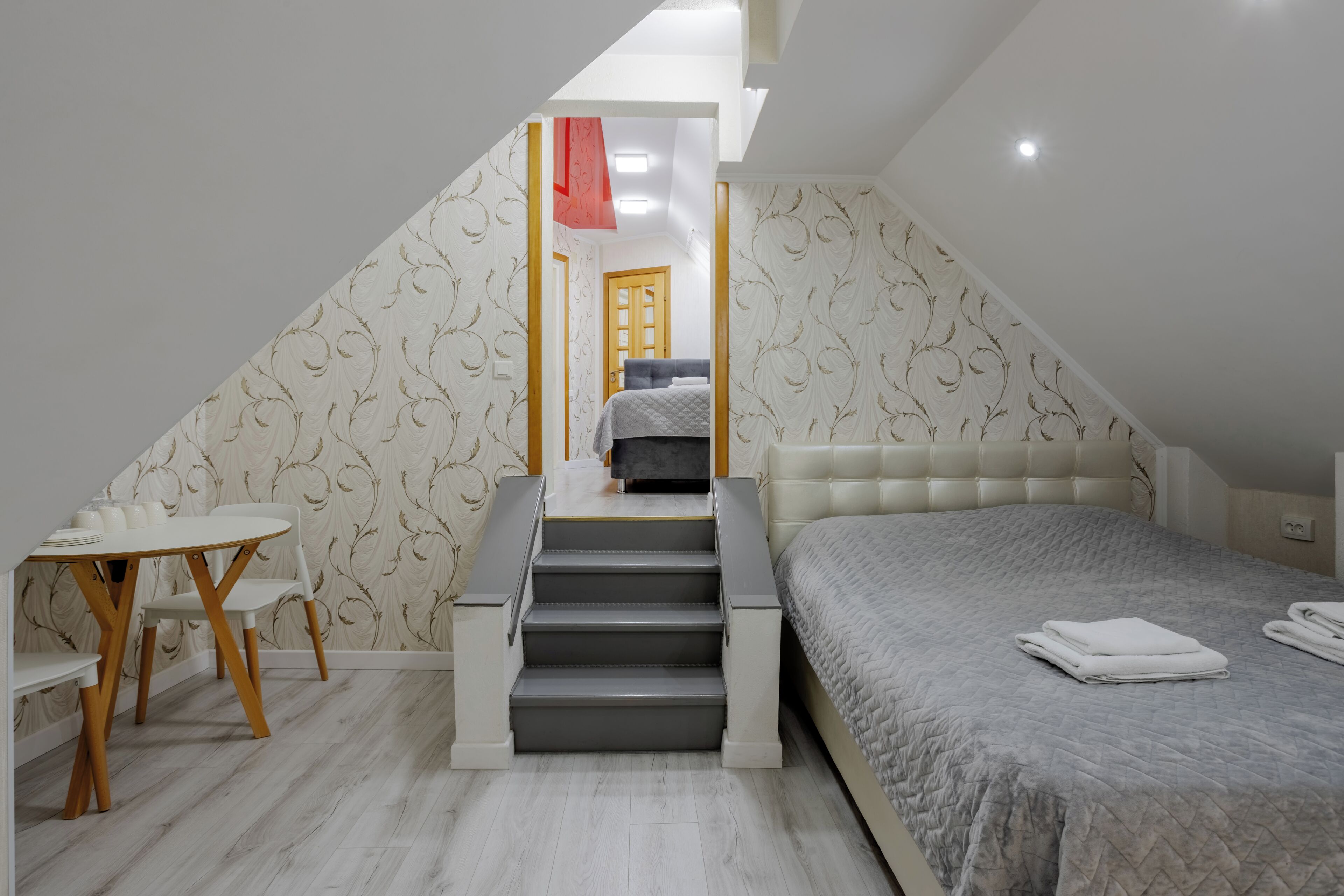 Un dormitorio con una cama, una mesa con sillas, una escalera y una puerta que da a otra habitación.