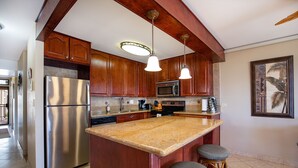 Cozinha com armários de madeira, eletrodomésticos de aço inoxidável, bancada de granito e dois banquetas.