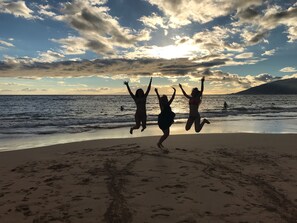 A beach scene with footprints leading to the water, a clear sky, and a sunset.