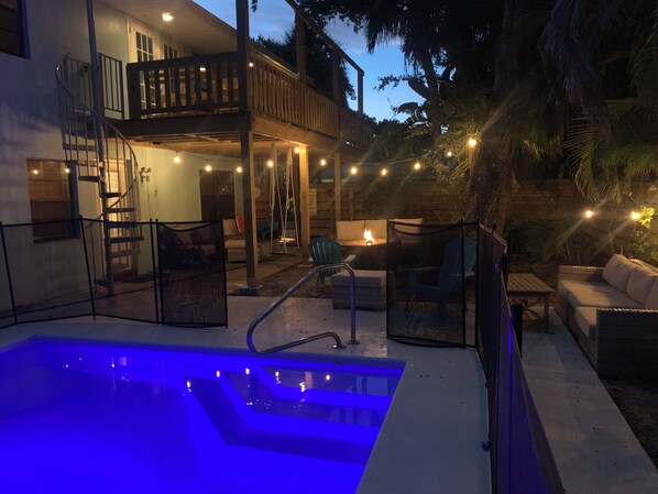 A pool area with a hot tub, outdoor seating, and a staircase leading to a balcony.