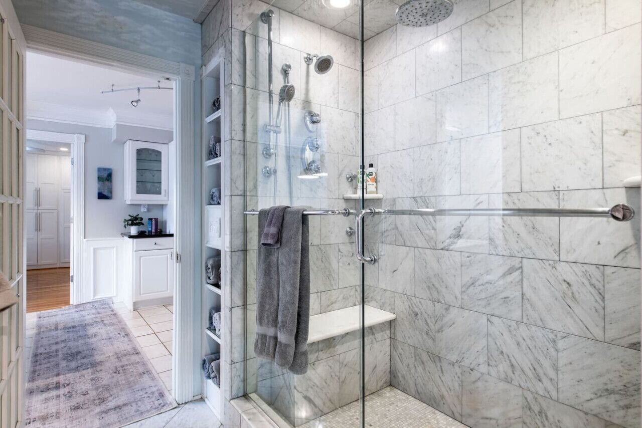 A modern bathroom with a glass-enclosed shower, marble tiles, and a towel rack.