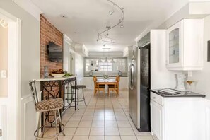 A kitchen with a brick wall, white cabinetry, a dining area with a table and chairs, and a refrigerator. - The Sweet Spot! - Live Like a Local (Saint Matthews)