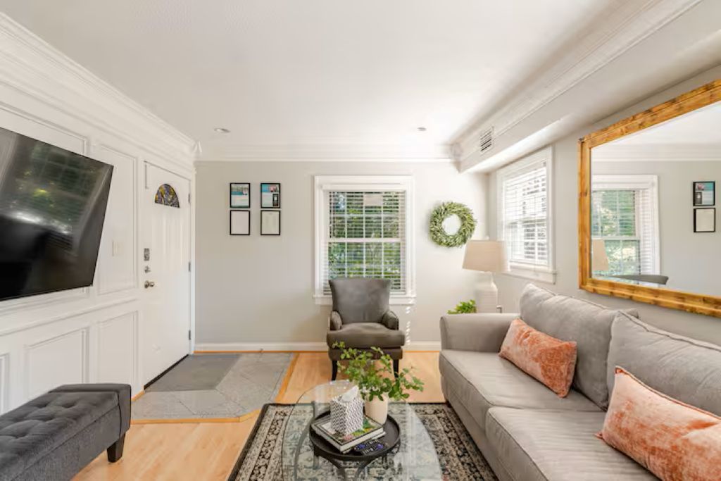 A living room with a television, a grey sofa, a grey armchair, and a coffee table with a plant.