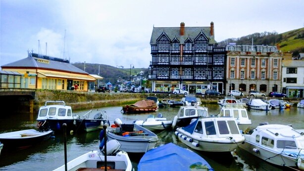 A harbor with several boats docked, a building with a black and white facade, and a yellow building with a sign. - Seahorse central Dartmouth Town 
 (Dartmouth)