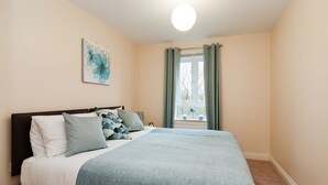 A neatly made bed with a blue blanket, a headboard, and a wall-mounted painting.