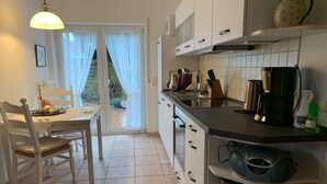 Una cocina moderna con armarios blancos, una mesa de comedor con sillas y un ventanal corredero que da a un jardín.