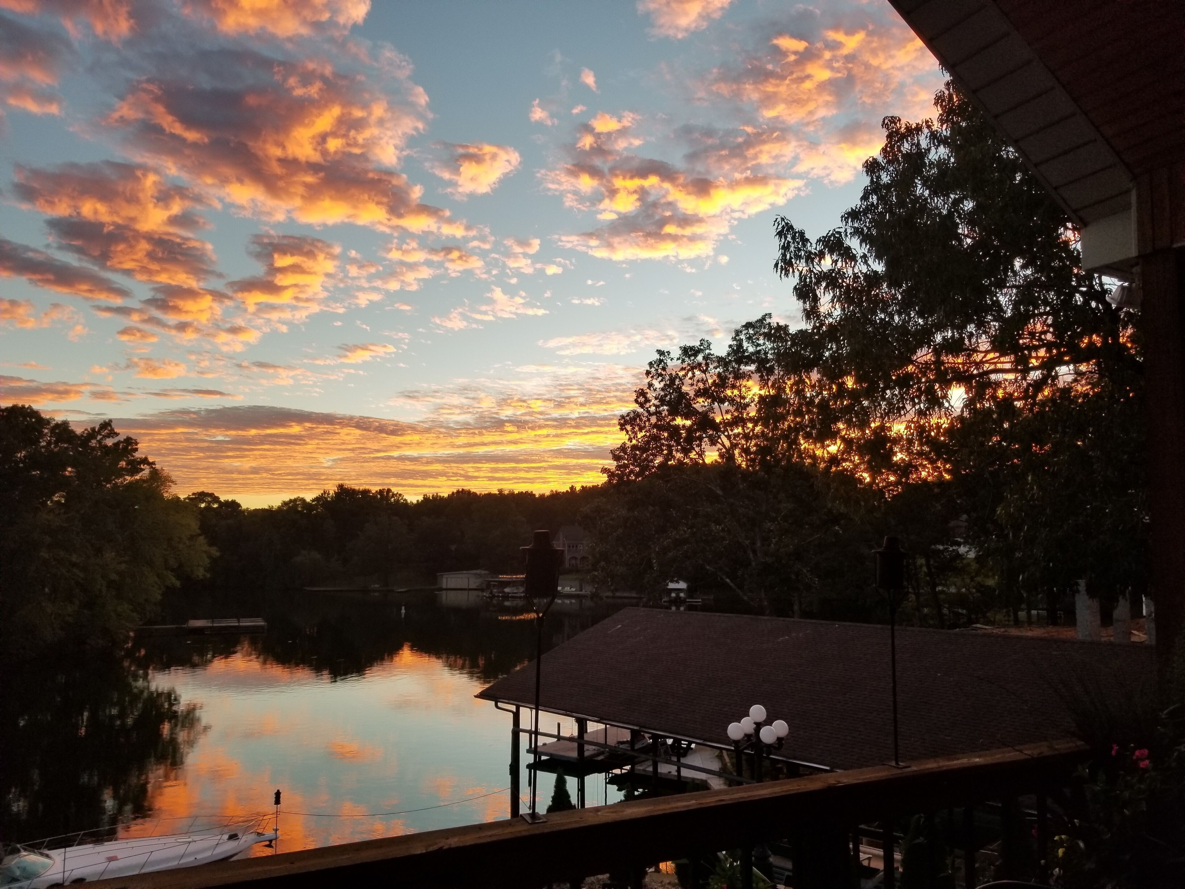 Une vue sur le coucher de soleil au-dessus d’un lac paisible, avec un quai et des arbres.