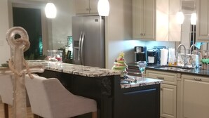 Een moderne keuken met een centraal eiland, barstoelen, roestvrijstalen apparatuur en hangende lampen.