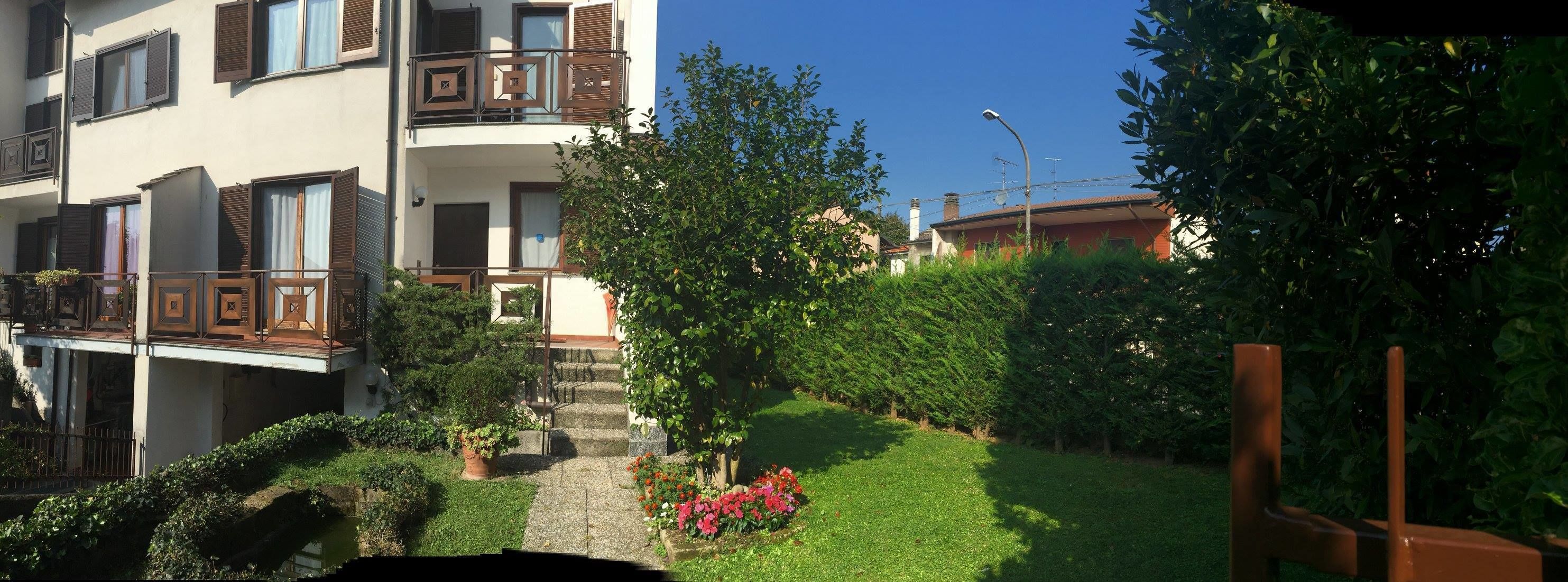 A multi-story residential building with balconies, a small garden with flowers, and a clear blue sky.