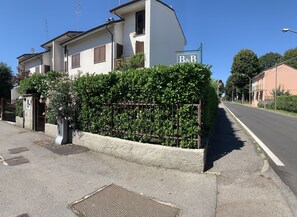 Un edificio residencial de dos pisos con entrada protegida por un portón, un letrero de B&B y un seto cuidado.