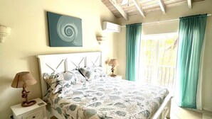 A bedroom with a bed, nightstands, a ceiling fan, a wall-mounted air conditioner, and a window with curtains. - 'Palm View', West Coast 3 bd/3.5br villa with Private Pool walk to beach/bars  (St James)
