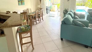 A dining area with a kitchen counter, wooden chairs, a teal sofa, and a ceiling fan. - 'Palm View', West Coast 3 bd/3.5br villa with Private Pool walk to beach/bars  (St James)