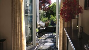 A doorway leading to a garden with a stone pathway, potted plants, and a red-leafed tree. - Keswick, Garden Apartment for 2. Excellent location.Convenient for all amenities (Keswick)