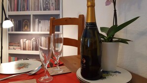A table with a bottle of champagne, two wine glasses, a plate with a floral design, a potted orchid, and a bookshelf in the background. - Keswick, Garden Apartment for 2. Excellent location.Convenient for all amenities (Keswick)