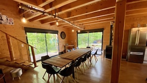 A wooden cabin interior with a dining table, chairs, a clock, and a refrigerator. - Le Hygge Chalet Gerardmer 1-10 Pers (Anould)