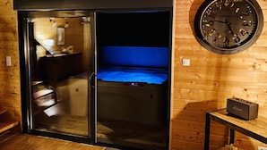 A room with a sliding door leading to a bed with a blue headboard, a round wall clock, and a small table with a radio. - Le Hygge Chalet Gerardmer 1-10 Pers (Anould)