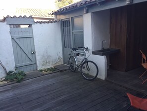 Ein Fahrrad vor einem Gebäude mit einer Holzterrasse, einer grauen Tür und einem kleinen Spülbecken.