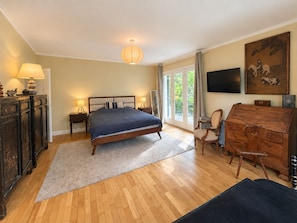 A bedroom with a bed, bedside tables, a dresser, a chair, a television, and a painting on the wall.