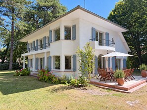 Una casa de dos pisos con un balcón, un patio con mobiliario exterior y un jardín bien cuidado.
