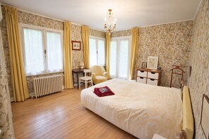 Une chambre d’hôtel avec un grand lit, un bureau, une chaise, un radiateur et un lustre.