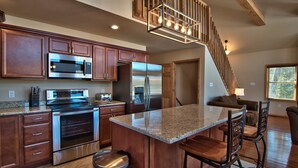 A kitchen with stainless steel appliances, wooden cabinets, a granite countertop, and a bar area with stools.