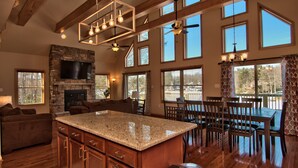 A spacious kitchen with a large island, wooden ceiling beams, and a stone fireplace.