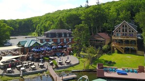 A lakeside resort with outdoor dining, a pool, and a large building with a deck.