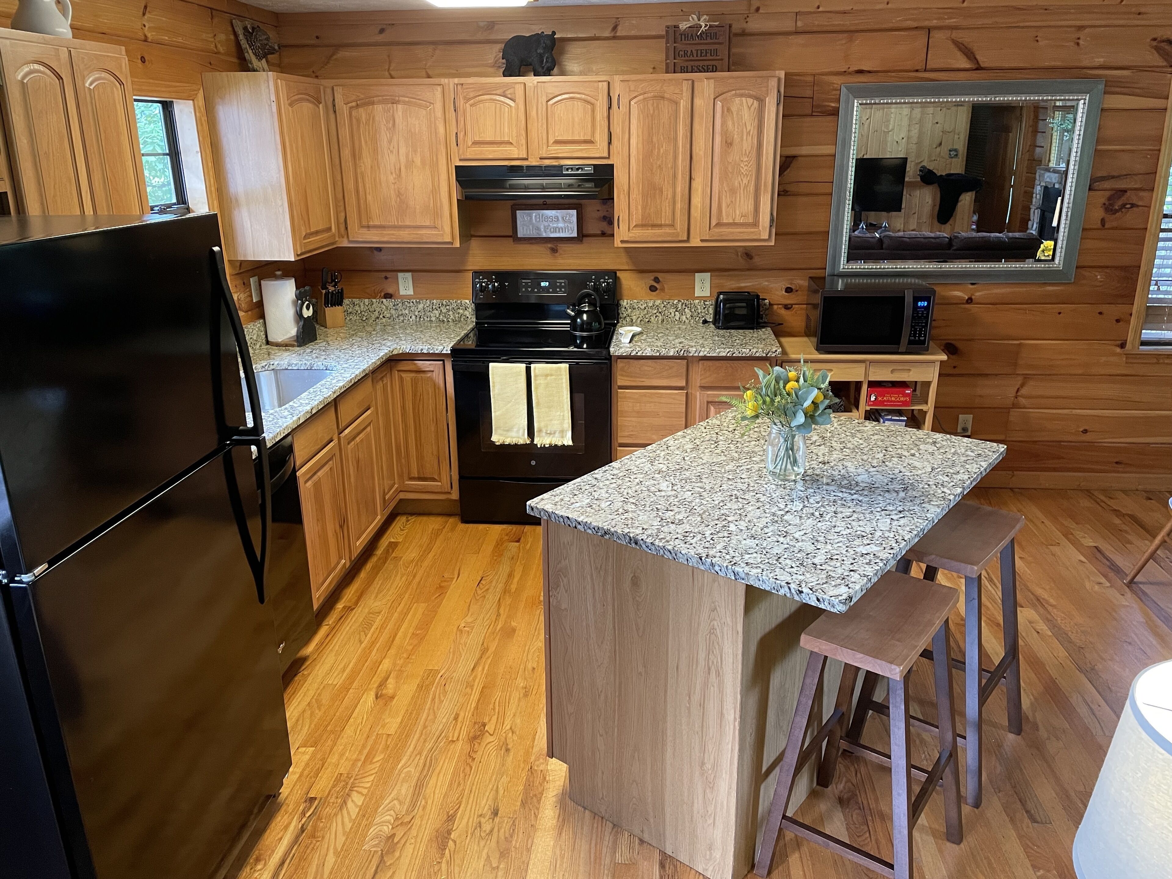 A kitchen with wooden cabinets, a black refrigerator, a stove, and a granite countertop.