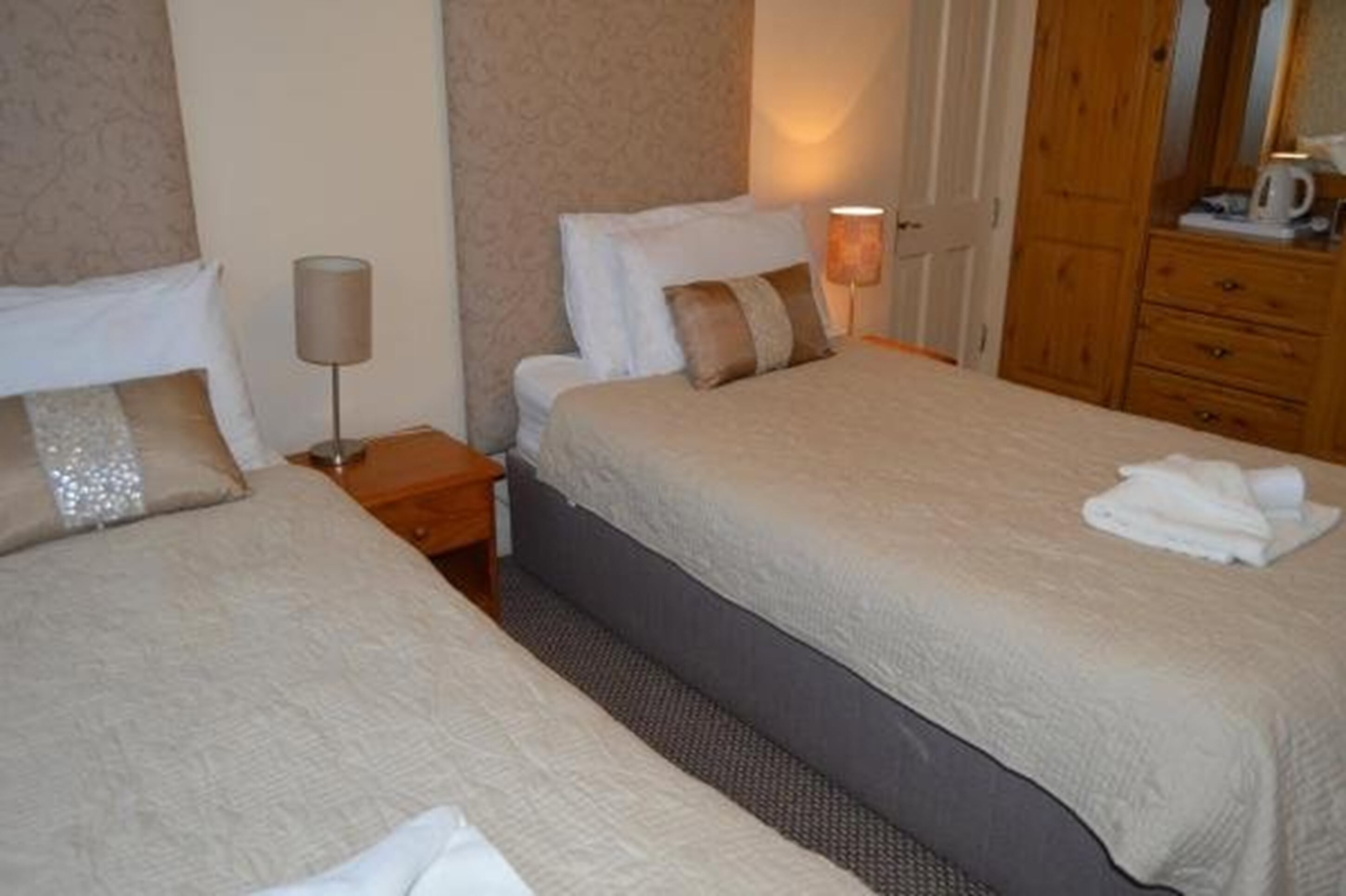 Ein Hotelzimmer mit zwei Betten, einem Nachttisch, einer Lampe, einem Holzschrank und einem Spiegel.