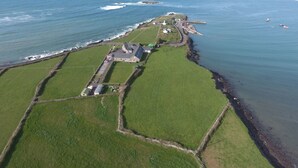 Vista aérea de una propiedad costera con un extenso campo cubierto de césped, una casa y un pequeño muelle.
